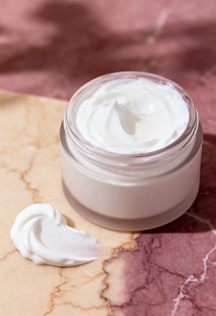 Jar of moisturizing cream with a dollop on marble